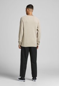 Beige knit sweater with long sleeves, crew neck, and a relaxed fit, paired with black tapered pants and black sneakers.