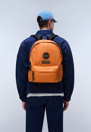 Homme portant une veste bleue et une casquette avec un sac à dos orange doté d'une poche avant et de deux curseurs de fermeture éclair noirs.