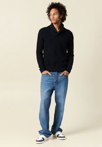 Maglione lavorato a maglia blu navy con colletto a scialle, abbinato a jeans blu chiaro con vestibilità comoda e sneakers bianche con accenti blu navy.