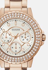 Roségoldene Chronograph-Uhr mit einem von Kristallen umgebenen Gehäuse, weißem Zifferblatt, drei Hilfszifferblättern und einem Metallgliederarmband.