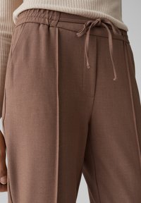 I joggers intrecciati marroni presentano una vita con laccetto, tasche laterali e una texture morbida con una vestibilità sartoriale.