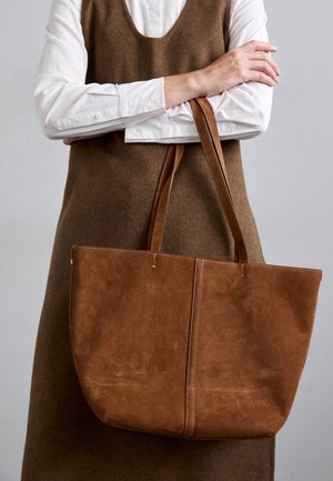 Sac cabas en suede marron avec de longues anses, arborant un design simple, des accents brodés et un intérieur spacieux.