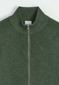 Pull en tricot côtelé vert avec un col montant et une fermeture éclair argentée à l'avant, présenté de la hauteur du col jusqu'à mi-torse sur un fond blanc.