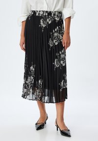 Jupon plissé noir avec des motifs floraux en blanc et gris, doté d'une taille élastique et d'un tissu léger et semi-transparent.