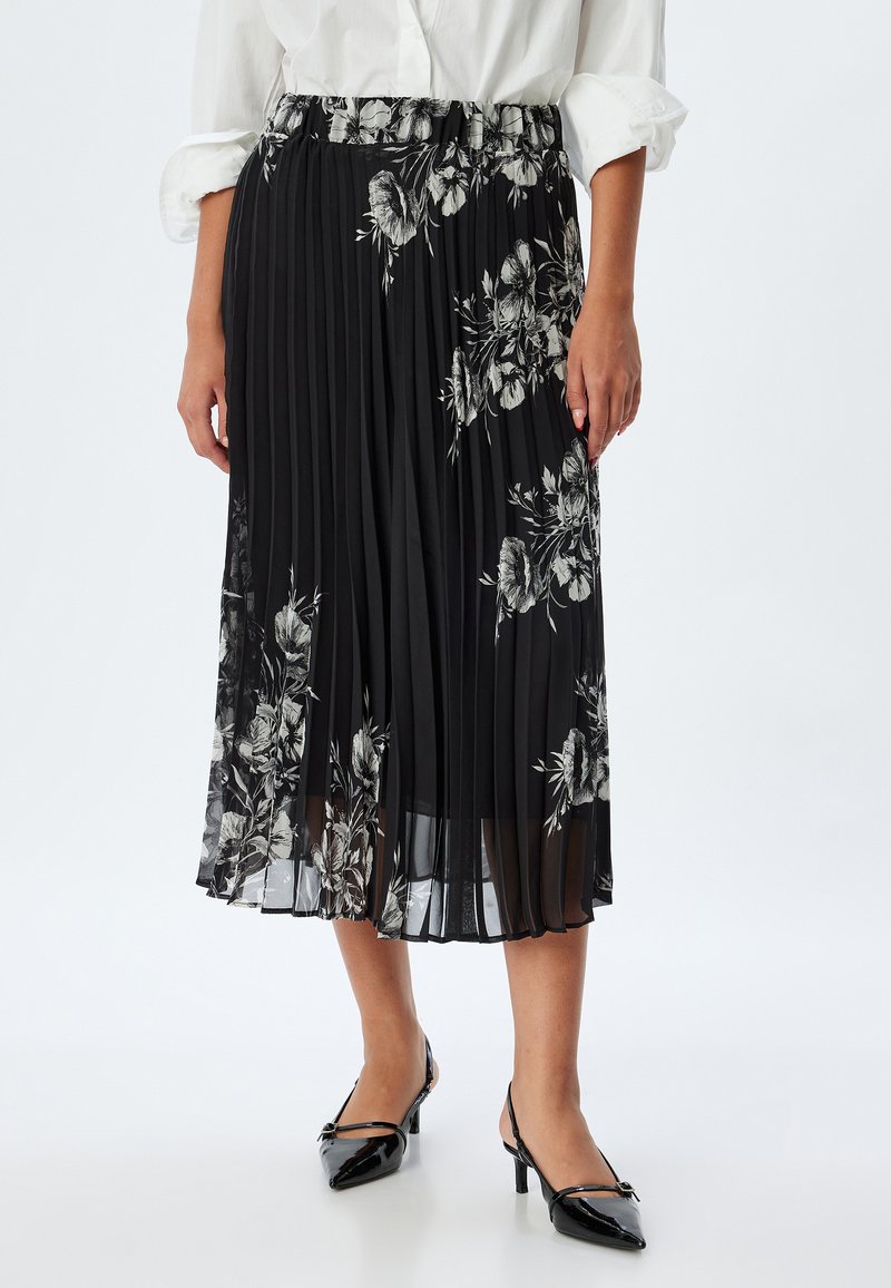 Jupon plissé noir avec des motifs floraux en blanc et gris, doté d'une taille élastique et d'un tissu léger et semi-transparent.