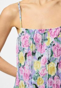 Top de tirantes con estampado floral que presenta textura plisada, con rosas rosas, amarillas y moradas sobre un fondo lila claro; con tirantes delgados y ajustables.