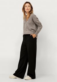 Grå V-hals sweater parret med brede sorte bukser og cremede chunky sneakers; sweateren har en blød tekstur og en afslappet pasform.