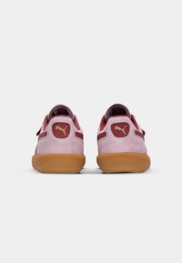 Rosa Wildledersneaker mit Gummisohle, die weinrote Akzente und ein goldenes Logo aufweist. Die Rückansicht zeigt eine glatte Textur und ein abgerundetes Design.