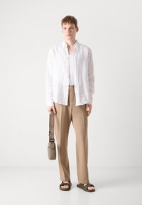 Hvit lin skjorte med lange ermer, beige bukser, brune sandaler og en lys brun skulderveske. Enkel design med avslappet passform og uten mønstre.