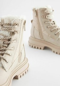 Beige winterlaarzen met een nepbont voering, gevoerde enkels, ronde neus en een robuuste rubberen zool; voorzien van een rits en stevige veters.