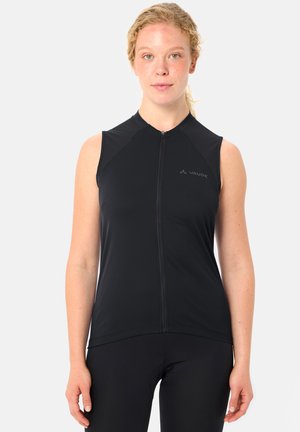 Frau mit lockigem blondem Haar, die ein ärmelloses schwarzes Vaude-Radtrikot mit Frontreißverschluss trägt und vor einem einfachen hellen Hintergrund steht.