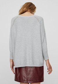 Pull en tricot gris à coupe décontractée, avec un ourlet et des manches côtelés, porté sur une jupe en simili cuir bourgogne.