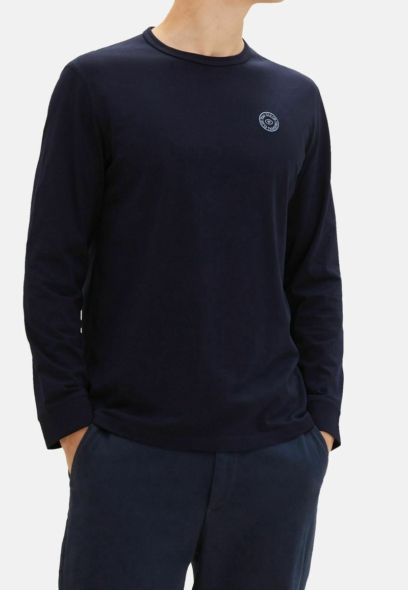 Marinen långärmad skjorta i mjukt material med rund hals; har en liten logotyp på bröstet och lätt ribbning vid ärmsluten.