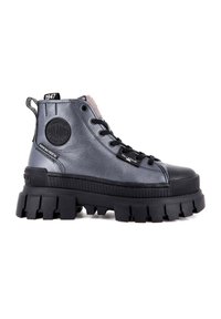 Botín alto metálico gris con suela negra gruesa, que presenta un parche redondo de logo y una etiqueta con marca. Parte superior de textil con cordones y puntera de goma.