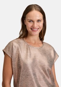 Top rose gold à manches courtes avec un design texturé en ribbes et un col rond, en tissu métallique brillant.