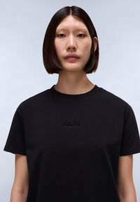 Černé bavlněné tričko s krátkým rukávem, s vyraženým logem "NAPA" na hrudi. Kulatý výstřih a hladká textura.