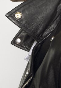 Černá kožená bunda s kovovými druky, viditelným šitím, zipem a měkkou vnitřní podšívkou. Detailní pohled na límec a klopu.