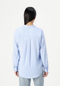 Light blue striped long-sleeve shirt with a buttoned collar and rounded hem, featuring vertical stripes in white and yellow accents.