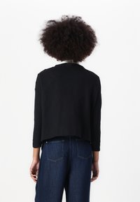 Black cropped sweater with a round neck, ribbed texture, and three-quarter sleeves, paired with high-waisted blue denim jeans.