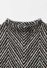 Nahaufnahme eines schwarz-weißen Strickstoffs mit einem Zickzackmuster, das eine V-Form bildet.