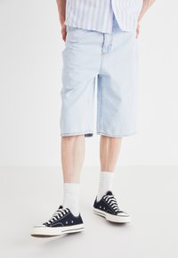 Light blue denim shorts with a relaxed fit, hitting just below the knees. Paired with black sneakers and white crew socks.