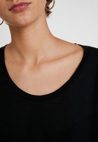 T-shirt preto com decote amplo em forma de barco, tecido leve, textura suave e design minimalista, destacando os ombros e a área do pescoço.