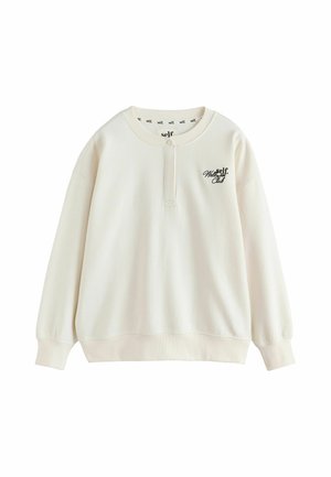 Cremefarbener Sweatshirt mit langen Ärmeln, geknöpftem Kragen, gerippten Bündchen und Saum sowie schwarzem "self. Wellness Club" Text auf der linken Brust.