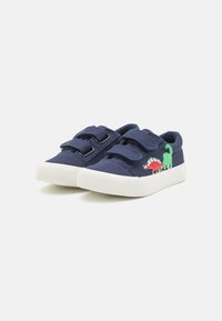 Chaussures en toile bleue avec deux sangles Velcro, semelle en caoutchouc blanche, ornées de motifs de dinosaures rouges et verts sur le côté.