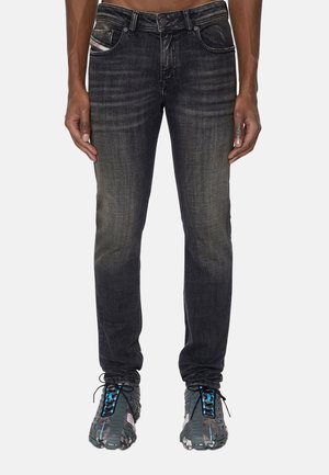 Vue de face d'une personne portant un jean slim noir délavé et des chaussures de sport foncées avec des détails bleus et blancs.