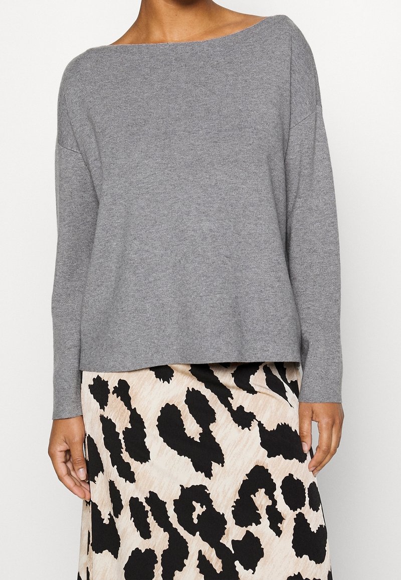 Femme portant un pull gris clair à manches longues et une jupe beige avec un grand imprimé léopard abstrait noir.