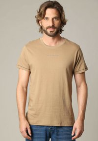 Beige katoenen t-shirt met korte mouwen, met een ronde hals en subtiele borduursels aan de voorkant. Gemaakt in combinatie met blauwe spijkerbroeken.