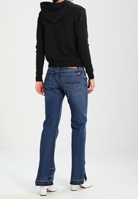 Sudadera negra con capucha combinada con jeans de mezclilla azul de corte recto, con aberturas laterales y textura ligeramente deslavada.