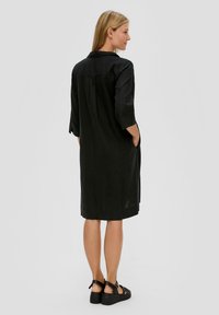 Zwarte linnen jurk met driekwartmouwen, voorzakken en een slanke snit, voorzien van een kraag en een rechte zoom.