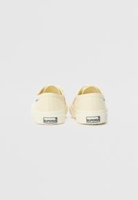 Canvas-sneakers i kremfarge med fargerike broderte detaljer på siden. Har en teksturert hvit gummisåle og en merket hælflik.