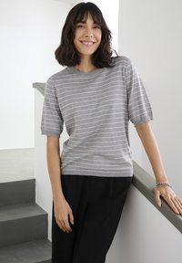 Hallide triibuline lühikeste varrukatega t-särk, ümar kaelus, pehme tekstuur, mustade pükstega kombineeritud. Lihtne disain, sobib igapäevaseks kandmiseks.