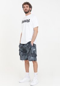 T-shirt bianca a maniche corte con testo grafico nero abbinata a pantaloni cargo mimetici grigi scuri dotati di tasche e corde di regolazione.