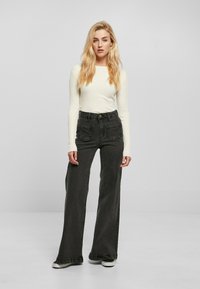 Jeans anchos negros con dos bolsillos frontales, cintura alta y dobladillo deshilachado, combinados con una camiseta ajustada blanca de manga larga de canalé.