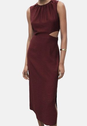 Robe midi bordeaux sans manches avec découpe sur le côté de la taille et encolure froncée portée par une personne avec un bracelet manchette doré au bras gauche.