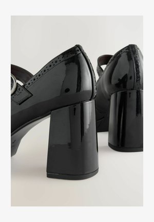 Scarpe con tacco in vernice nera, dotate di un tacco a blocco chunky, caratterizzate da perforazioni decorative e una cinturino regolabile con un fibbia circolare.