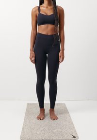 Czarny sportowy stanik z cienkimi ramiączkami oraz legginsy o wysokim stanie, wykonane z gładkiego, elastycznego materiału. Bez butów na teksturowanej szarej macie.