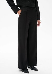 Zwarte wijdlopende broeken van soepel materiaal, met een hoge taille, zijzakken en een scherpe vouw aan de voorkant.