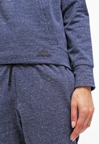 Sweat-shirt bleu marine en tissu texturé, avec une poche avant et un logo Adidas noir. Comprend des poignets et un ourlet élastiques.
