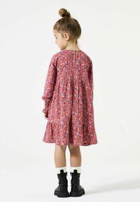 Rotes Kleid mit Paisley-Muster, langen Ärmeln, gerafftem Rock und einem Schlüssel-Lochverschluss im Rücken. Schwarze Knöchelstiefel mit weißen strukturierten Socken.