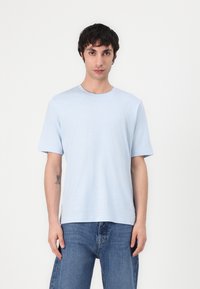 Light blue short-sleeve t-shirt made of soft fabric, featuring a round neck and relaxed fit, worn with blue denim pants.