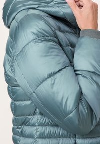 Chaqueta acolchada de un suave color azul verdoso con un exterior brillante. Presenta costuras horizontales, una capucha y puños elásticos para un ajuste ceñido.