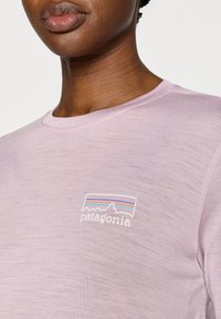 Ανοιχτό μωβ κοντομάνικη μπλούζα κατασκευασμένη από απαλό ύφασμα, με λογότυπο βουνού με πολύχρωμες ρίγες στην αριστερή πλευρά του στήθους.