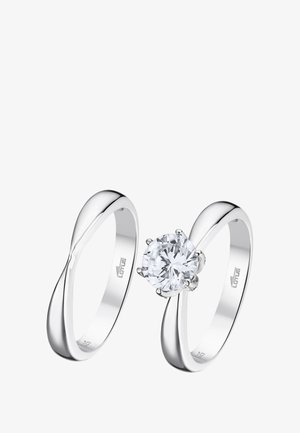 Two silver rings. One features a round, clear gemstone set in a multi-prong setting; the other has a smooth, twisting band design.