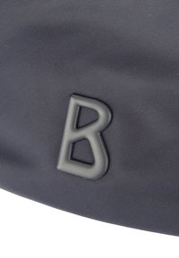 Temno sivi tkanini prikazuje izbočeno, mat črno črko "B" s posebno, kotno zasnovo. Vidna je teksturirana površina.