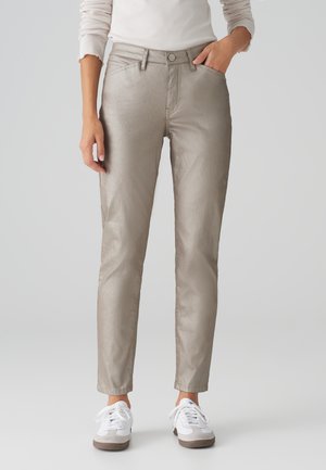Helle beige metallische Ankle-Hosen mit leichter Passform, ausgestattet mit Fronttaschen und einem Knopfverschluss. Kombiniert mit weißen und grauen Sneakers.