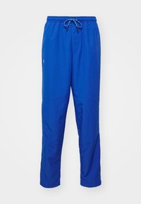 Pantalon de sport bleu avec ceinture élastique et cordon, en tissu léger, avec un petit logo Under Armour sur la cuisse gauche.
